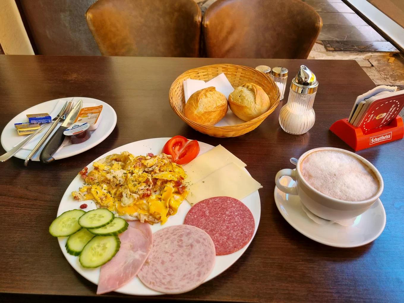 Ein Frühstücksteller mit Rührei, Aufschnitt, Käse, frischem Gemüse, Brötchen und Cappuccino